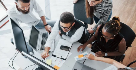 5 people in an office working in front of a computer referencing Scaling with dedicated development teams