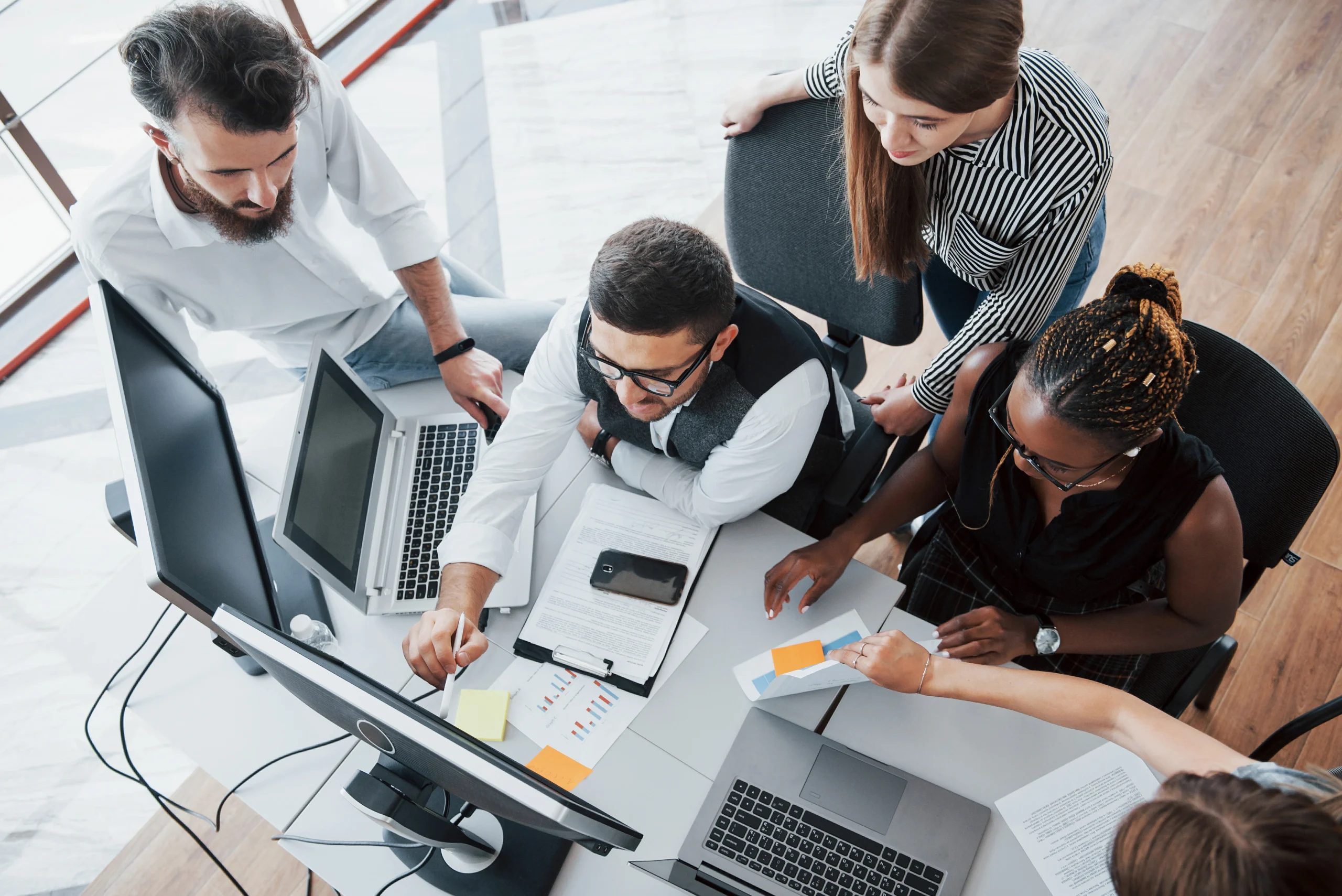 5 people in an office working in front of a computer referencing Scaling with dedicated development teams