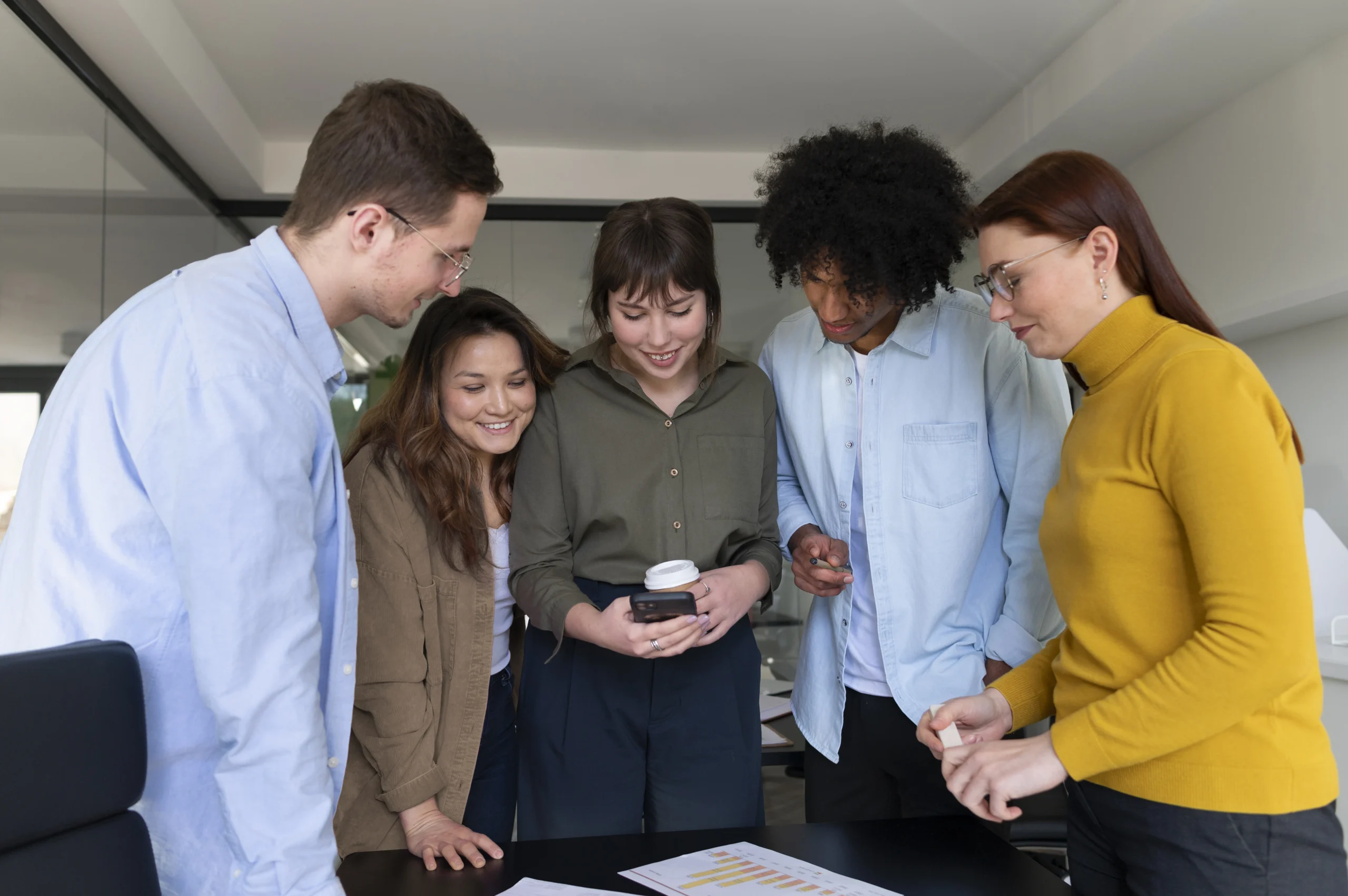 5 people in an office and they are all focused on a cell phone that the person in the center is holding