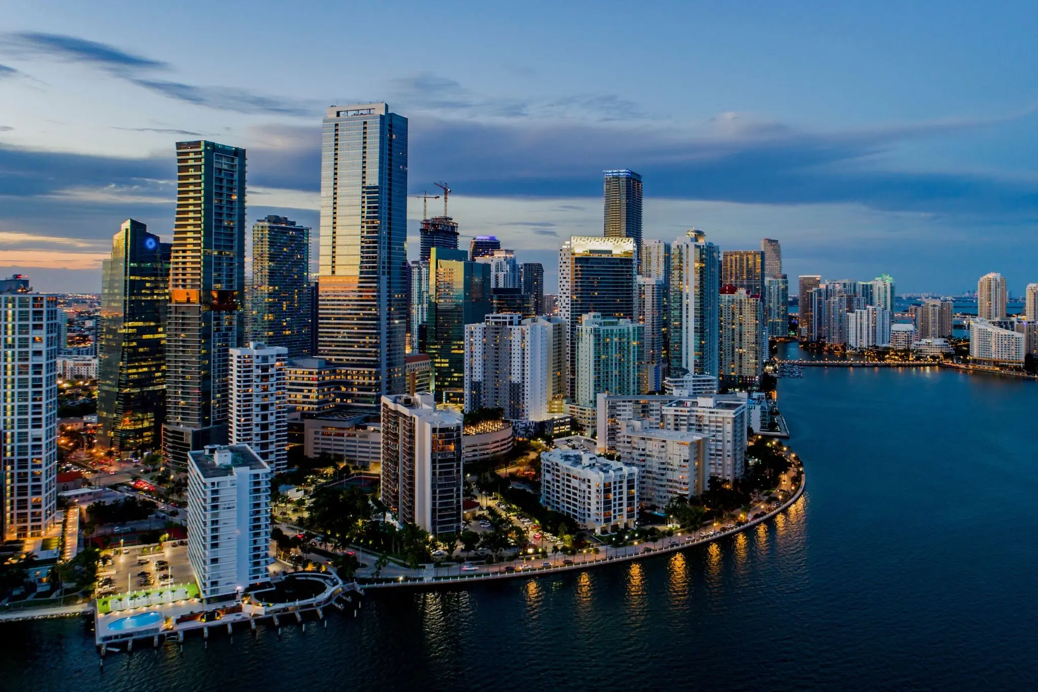 Miami’s waterfront skyline at dusk, featuring tall, illuminated buildings reflecting on the water.
