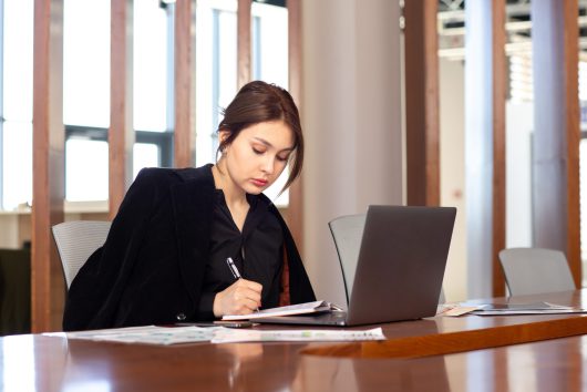 front-view-young-attractive-businesswoman-black-shirt-black-jacket-using-her-silver-laptop-writing-down-notes-working-inside-her-office-work-job-building