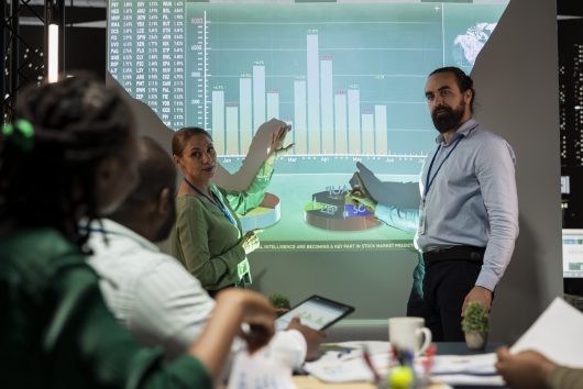 Management team sharing insight on statistics in night corporation meeting Management team sharing insight on statistics in night corporation meeting, providing initiatives to enhance operational performance metrics. Group of business associates in boardroom.