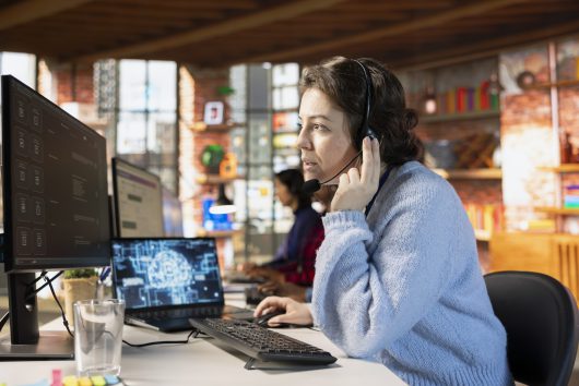 Woman doing customer support job using AI to summarize clients issues Call center worker wearing audio headset in office using AI to generate call scripts during conversation with customers. Woman doing customer support job using AI to summarize clients issues